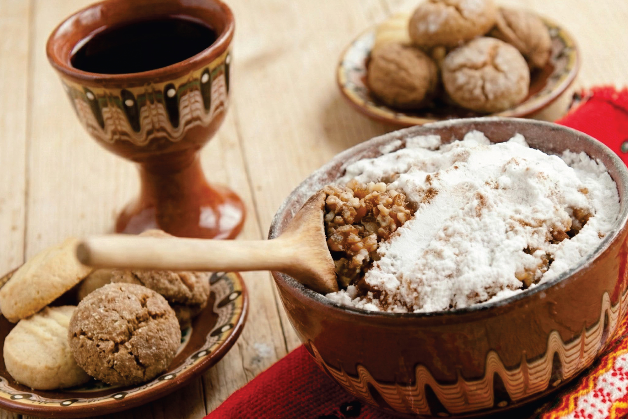 Купа с коливо, поръсено с пудра захар, чаша вино и чиния с бисквити.