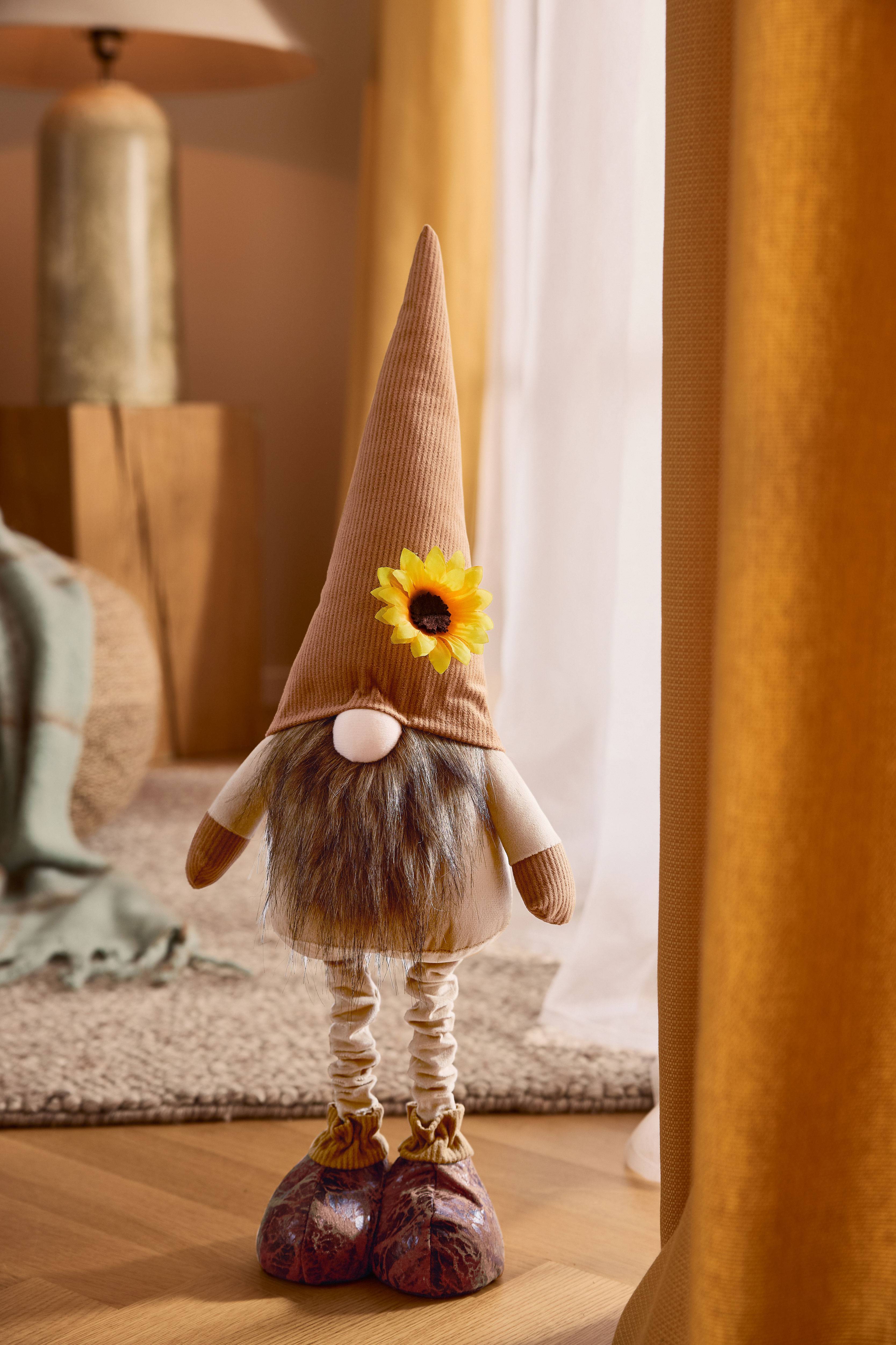 Плюшен гном с кафява заострена шапка, брада и слънчоглед, в уютна обстановка.